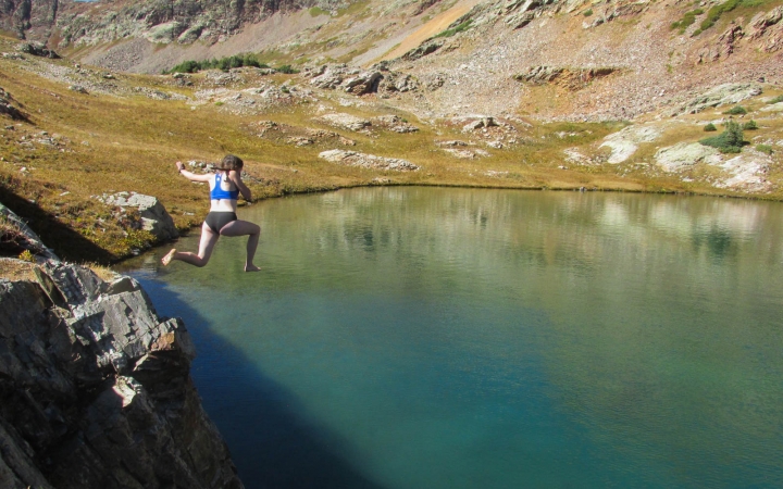 A person jumps off a rock into a body of water.